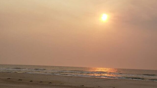 Foto do sol sobre a praia no litoral sul, com um céu encoberto pela fumaça das queimadas no Pantanal brasileiro em 2020, fazendo referência a um indicador.